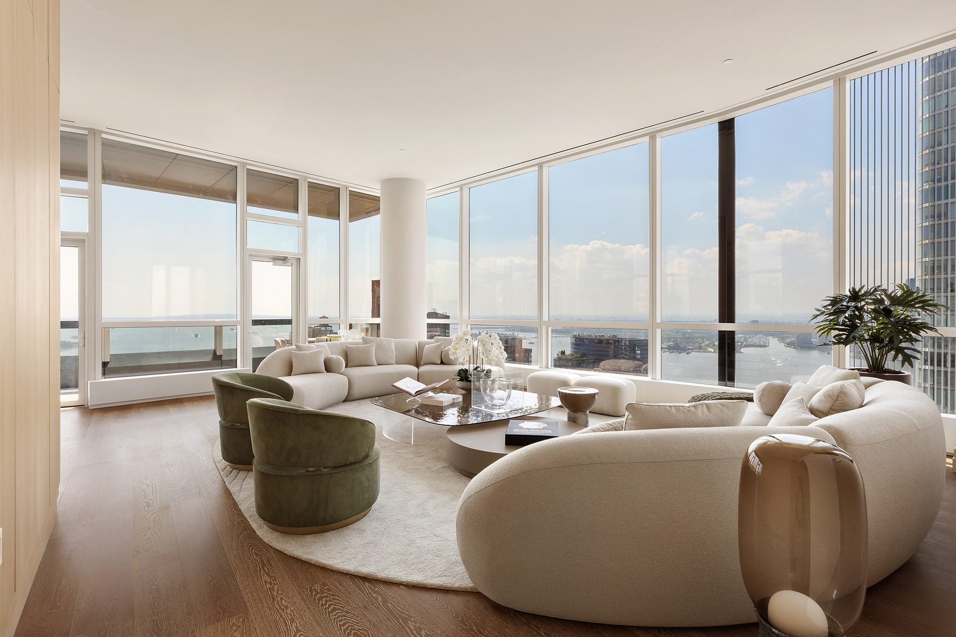 The Penthouse great room with curved seating and a corner wall of glass framing the harbor