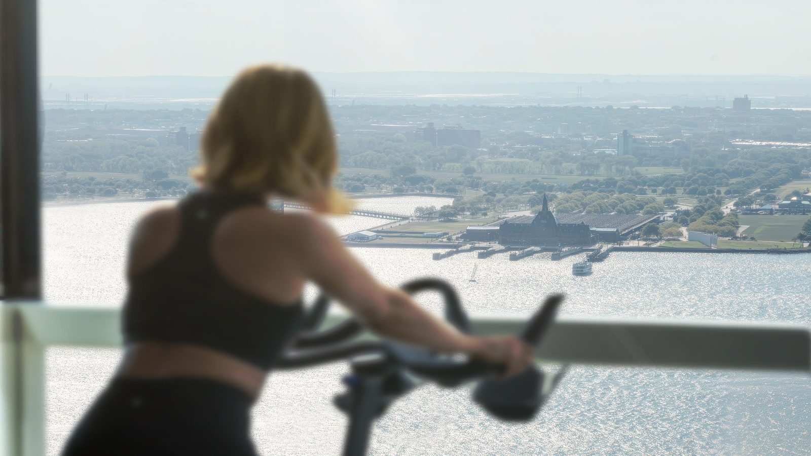 Resident on a bike in the fitness center, harbor and Statue of Liberty beyond