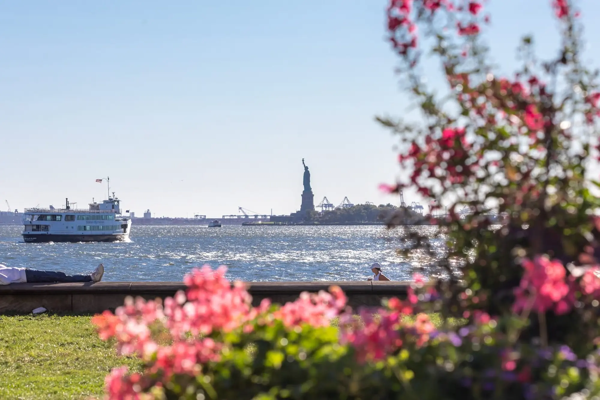 The Statue of Liberty across the harbor, framed by flowers in a waterfront park