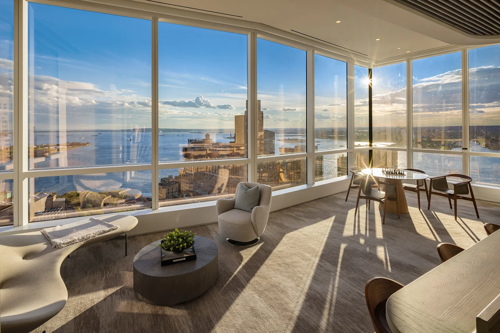A sunlit corner lounge with chess table and panoramic harbor views