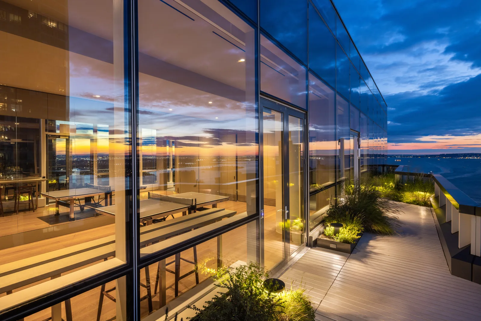 The glass-walled sky lounge and planted terrace at twilight