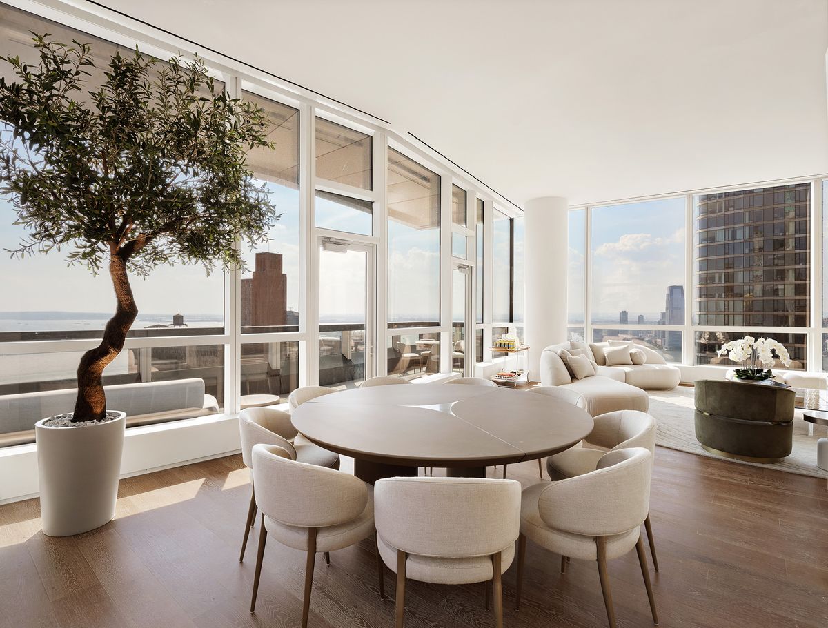 The dining room with a round table, sculptural olive tree, and floor-to-ceiling glass